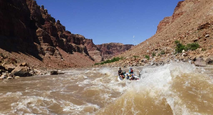 People paddle a raft through whitewater framed by tall canyon walls. 